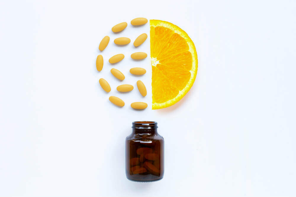 Vitamin C bottle and pills with orange fruit on white